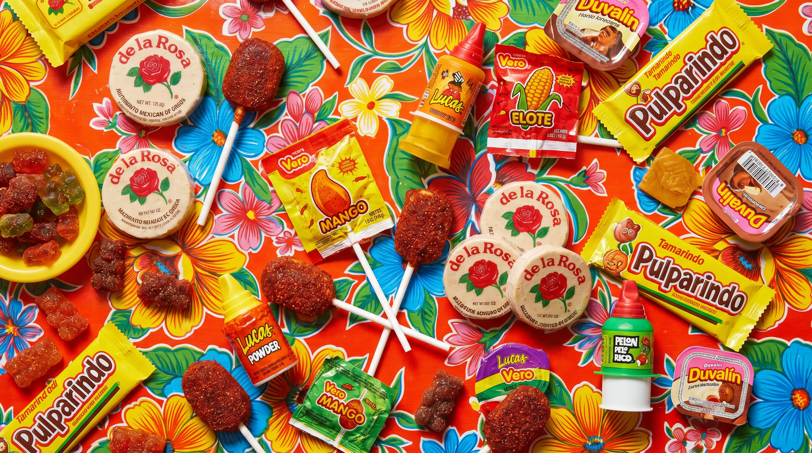 A colorful spread of authentic Mexican candy including Mazapan discs, chili-coated lollipops, Pulparindo tamarind bars, and chamoy gummy bears arranged on a bright surface