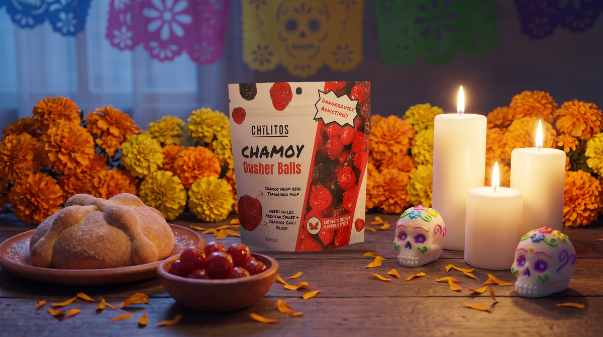 Chilitos Chamoy Gusher Balls 6 oz bag on a Día de los Muertos party table with orange marigolds, pan de muerto, lit candles, sugar skulls and papel picado